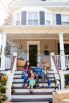 Family Sitting On Steps Of New Home On Moving In Day