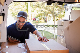 Courier With Digital Tablet Checking Packages In Van