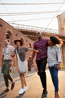 Group Of Friends Walking By Brooklyn Bridge In New York City
