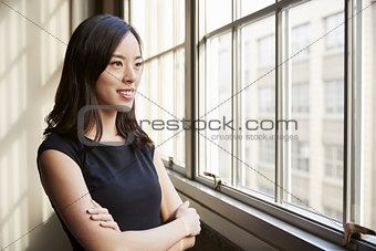 Smiling young Chinese business woman looking out of window