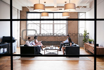 Business people in lounge meeting area, seen through window