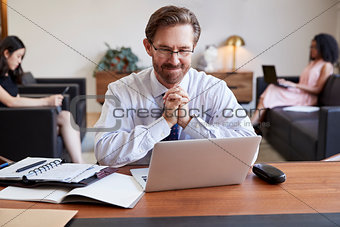 Businessman using laptop at desk, colleagues in background