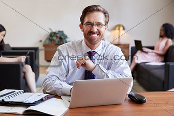 Businessman using laptop at desk smiling to camera