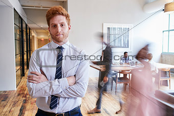 Portrait of young red haired man in a busy modern workplace