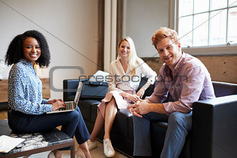 Three young colleagues at a casual work meeting look to camera