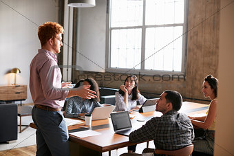 Young man standing to address colleagues at a work meeting