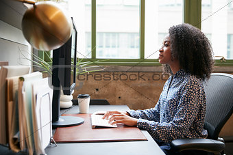 Black woman working at a computer in an office, side view