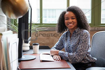 Black woman at a computer in an office smiling to camera