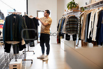 Young Hispanic man looking at clothes on a rail in a shop
