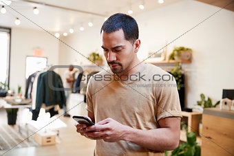 Young Hispanic man using smartphone in a clothes shop