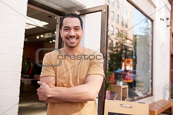 Young Hispanic shop owner smiling to camera outside his shop