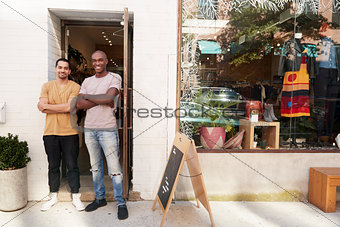 Two young men smiling to camera outside their clothes shop