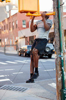 Young black man doing chin ups in Brooklyn street, vertical