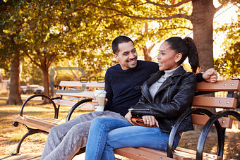 Young Hispanic couple sitting on bench in Brooklyn park
