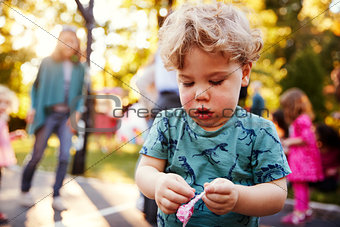 Toddler boy unwrapping a lollipop outdoors