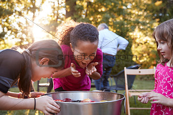 Three young girls apple bobbing at a backyard party
