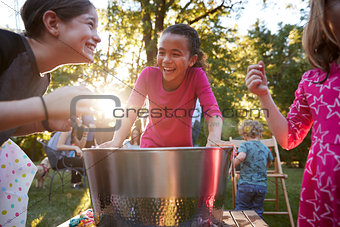 Three young girls have fun apple bobbing at a backyard party