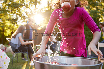 Pre-teen girl apple bobbing, with apple in mouth, close up