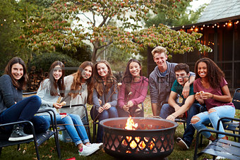 Teenage group sitting around a fire pit smiling to camera