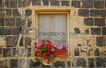 Stone house, window and blooming geranium