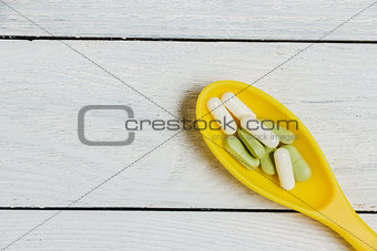 Assortment of Pills, Tablets and Capsules in Yellow Spoon on Wooden Table.