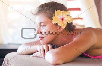 beautiful young woman with flower in hair enjoying her time in tropical spa
