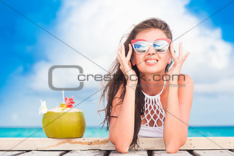 long haired woman in bikini and sunglasses with fresh coconut cocktail relaxing on tropical beach