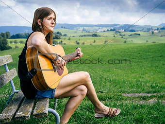 Woman playing guitar on a park bench