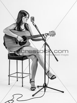 Young woman sitting on stool playing acoustic guitar