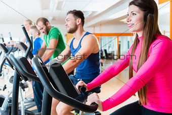 Men and women on cardio bikes in gym