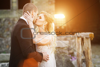Bride and groom kissing near the lightened by sunset building