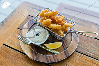 Calamari (Crispy Squid) with sauce and lemon in wooden plate with a fork on the wooden table. Selective focus.