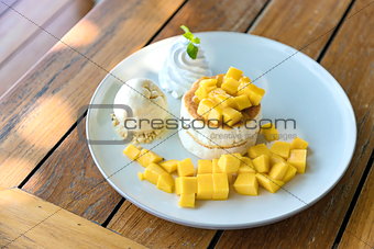 Mango and vanilla ice cream with fluffy cake in white plate on the wooden table. Selective focus.