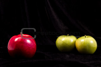 one red and two green apple on black background