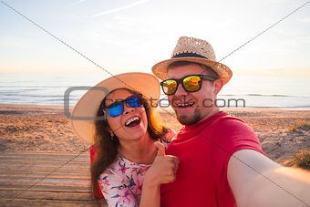 Happy traveling couple in love taking a selfie on phone with suitcases at the beach on a sunny summer day