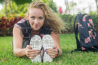 Blonde girl, does exercise sitting on the grass, stretches her body facing camera