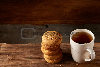 White porcelain mug of tea and sweet cookies on piece of wood over wooden background, top view, selective focus