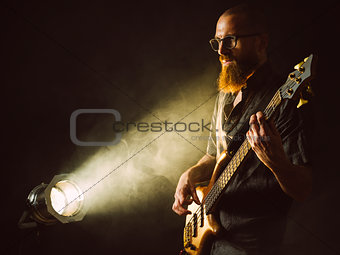 Bearded man playing bass guitar with spotlight