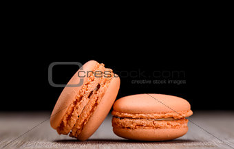 Two orange macaroons on wooden background