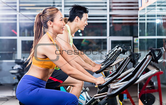 Sportive Asian couple doing indoor cycling in gym