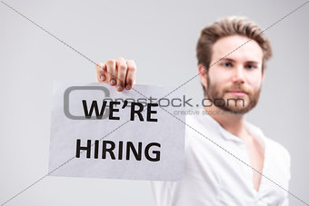 Bearded man holding up a We're Hiring sign