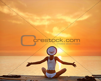 beautiful sexual woman in white hat and bikini on a wooden pier against the sea and sunset
