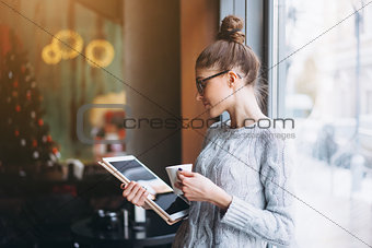 Young girl looking at tablet and smiling in cafe with big window.