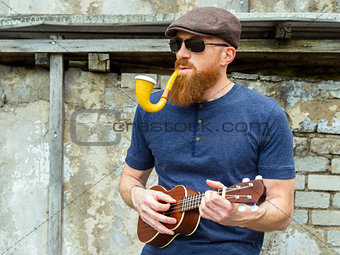 Man with beard playing ukulele and smoking a pipe