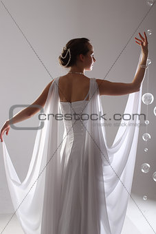 girl in white and with raised hands, attached to the floor dresses. the bride in a dress in Greek style. brunette in pearl jewelry lowered her head. The woman looks like a bird or a bat