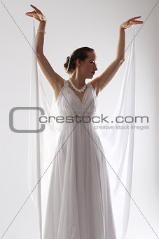 girl in white and with raised hands, attached to the floor dresses. the bride in a dress in Greek style. brunette in pearl jewelry lowered her head. The woman looks like a bird or a bat