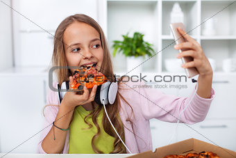 Young teenager girl eating pizza in the kitchen - making a selfi