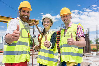 Three colleagues in a construction team showing thumbs up