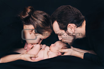 newborn baby lying on the hands of parents on a black background.