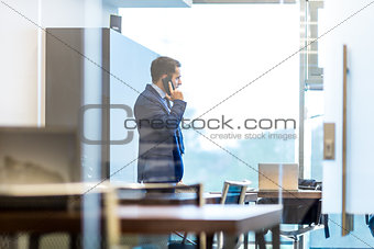 Businessman talking on a mobile phone while looking through window.